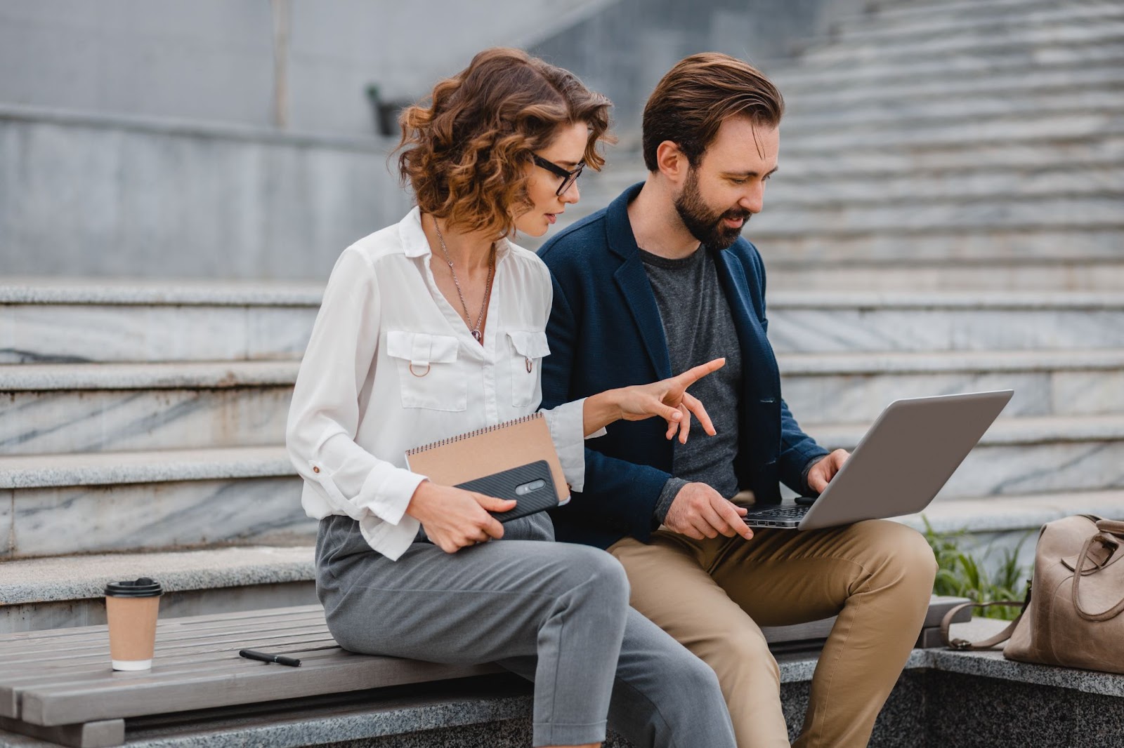 Man and woman sitting on stairs and working together on laptop